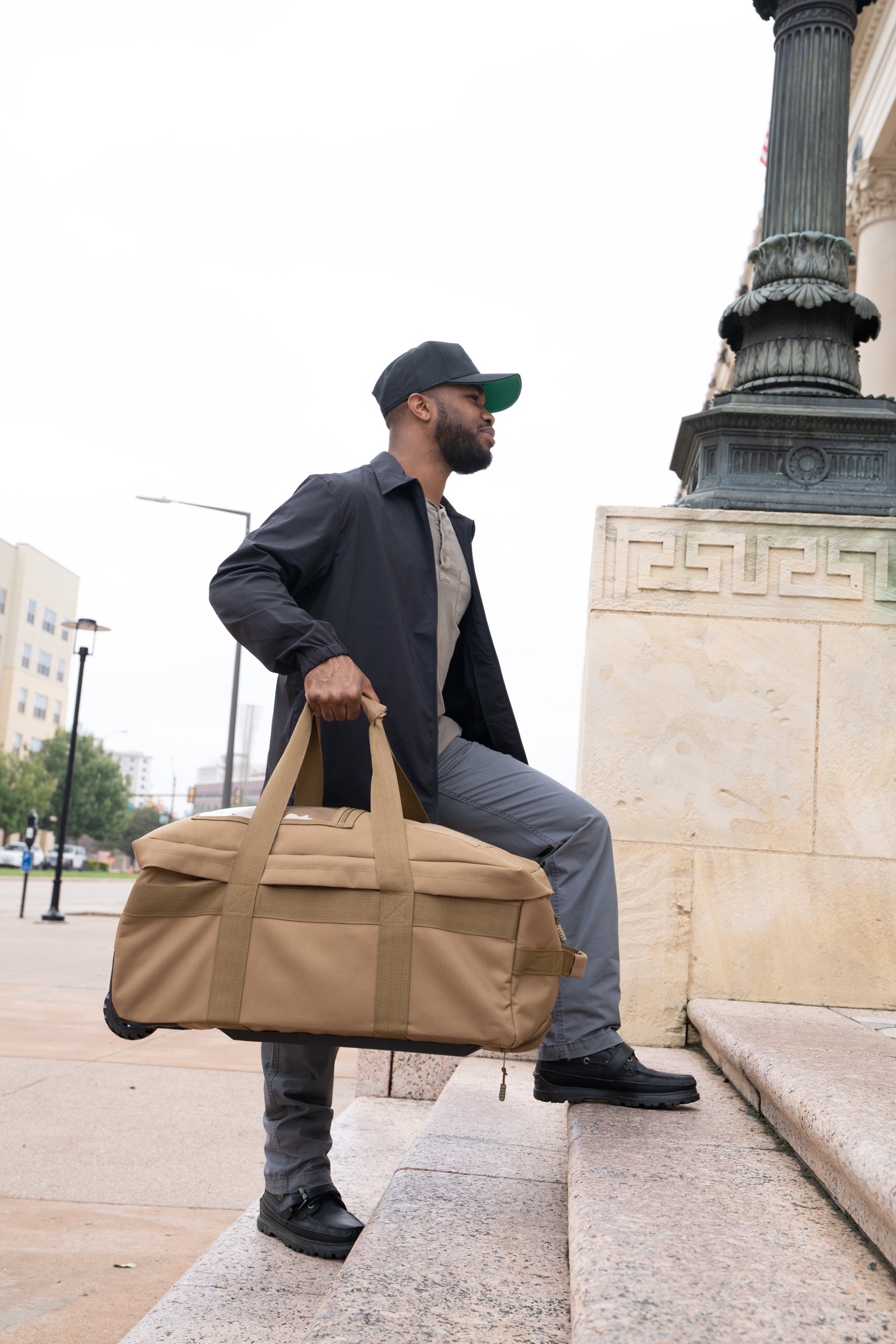 Man carrying coyote brown Mini Buffalo Rolling Duffel.