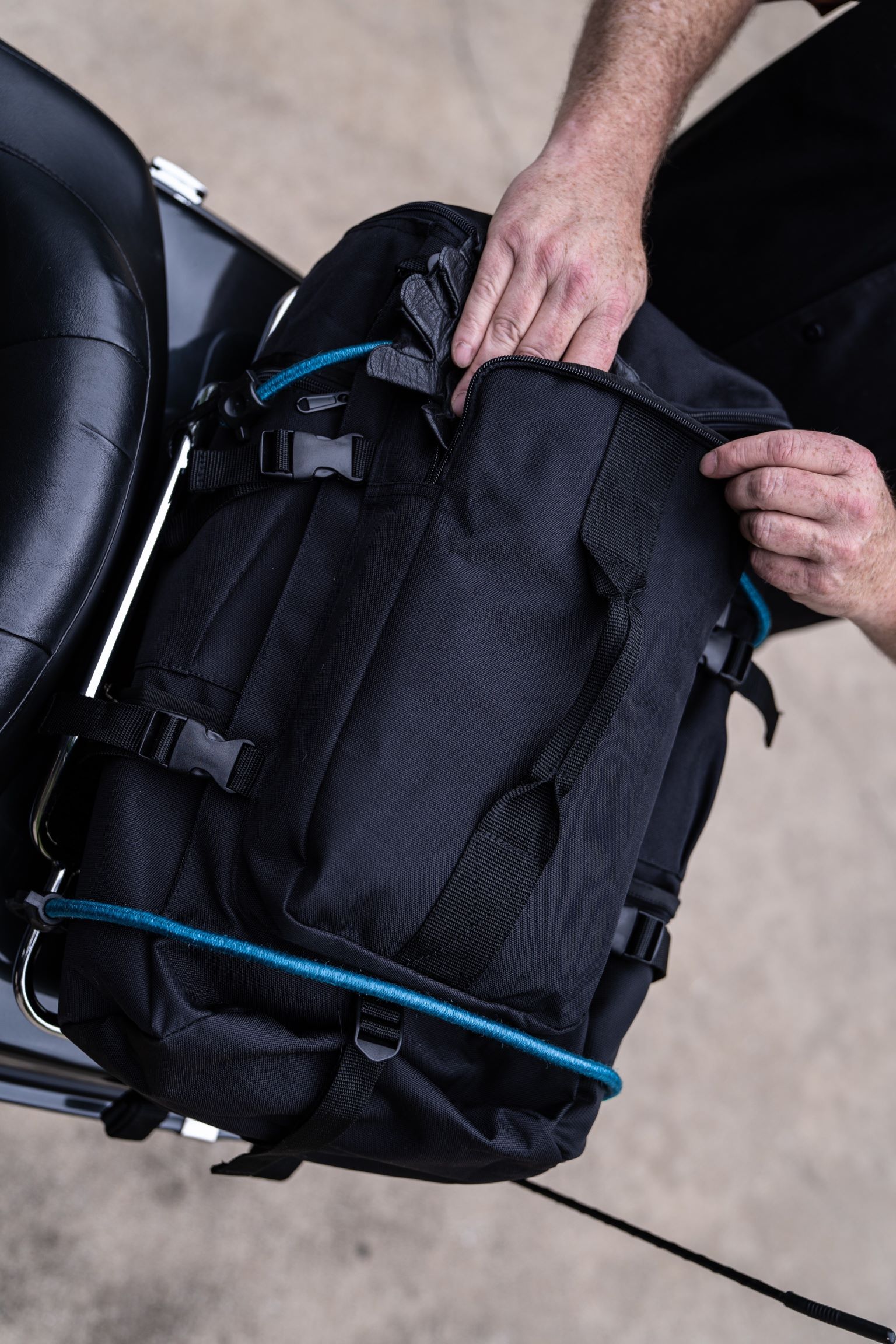 Man packing black Top Load Duffel on the back of motorcycle.